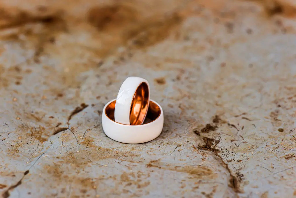Two Matching Couple Rings White and Rose Gold Ceramic Rings on Rustic Backdrop