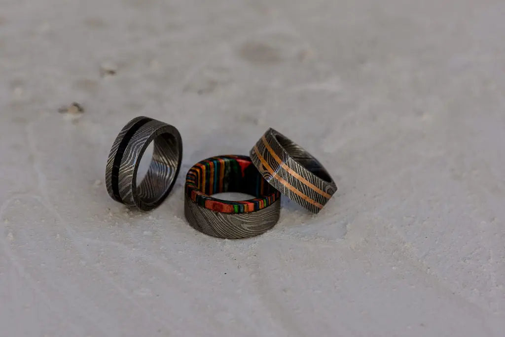 Three Damascus rings with inlays on dusty backdrop